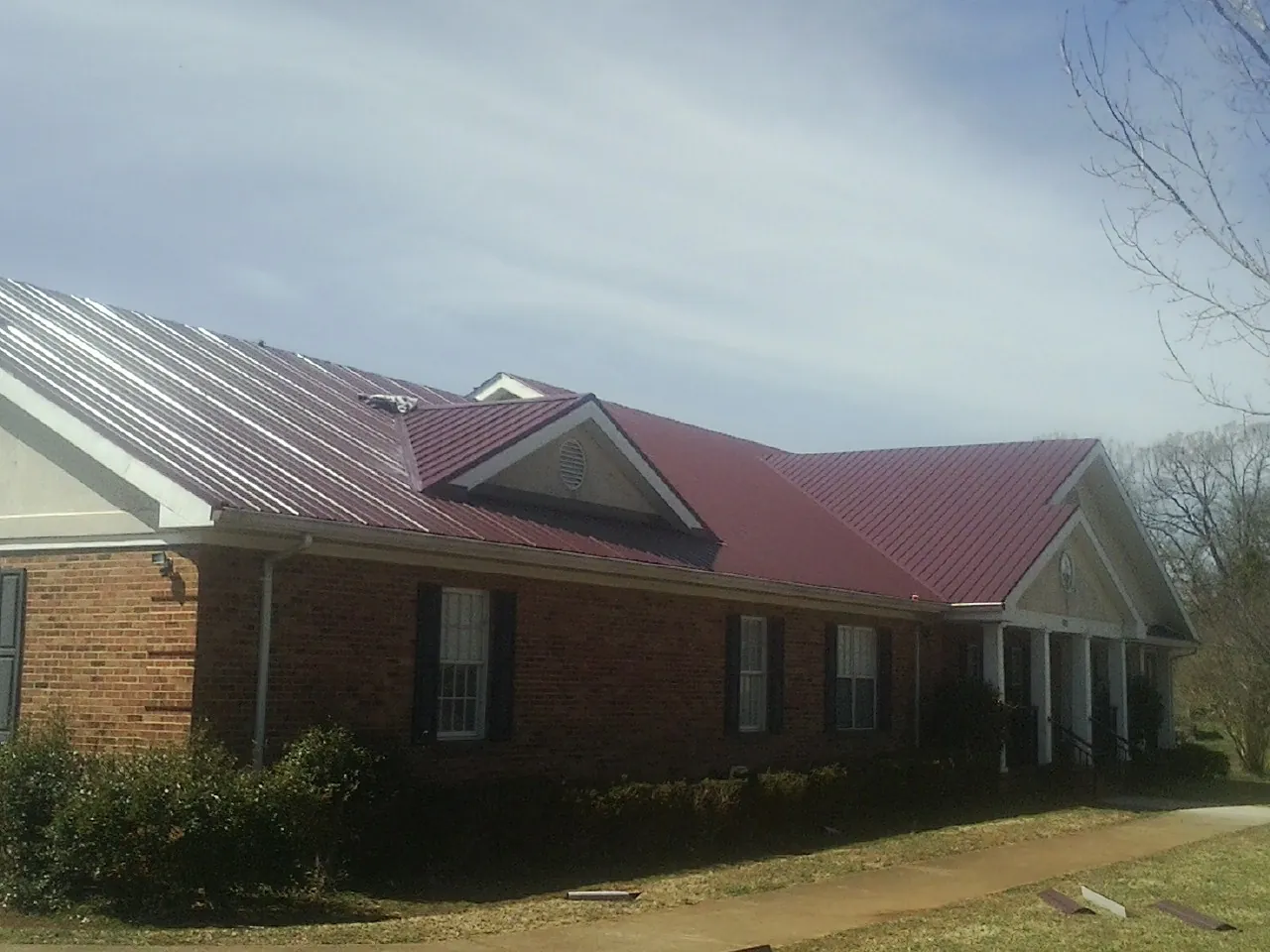 Red metal roof with gabled entries on a long brick building, from a Hail Damage Roof Repair job in White Salmon