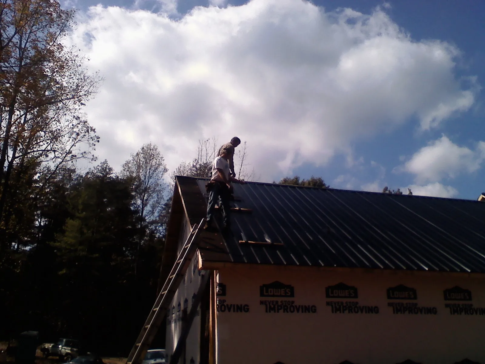 Roofer fastening dark metal panels high against a cloudy sky, from a Roof Inspection job in White Salmon
