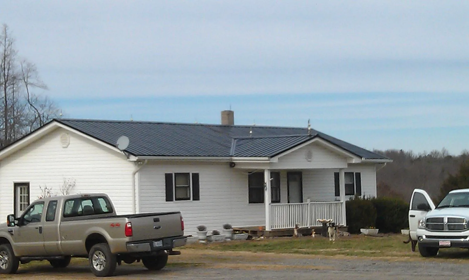 Finished dark metal roof on a white ranch home with work trucks parked in White Salmon