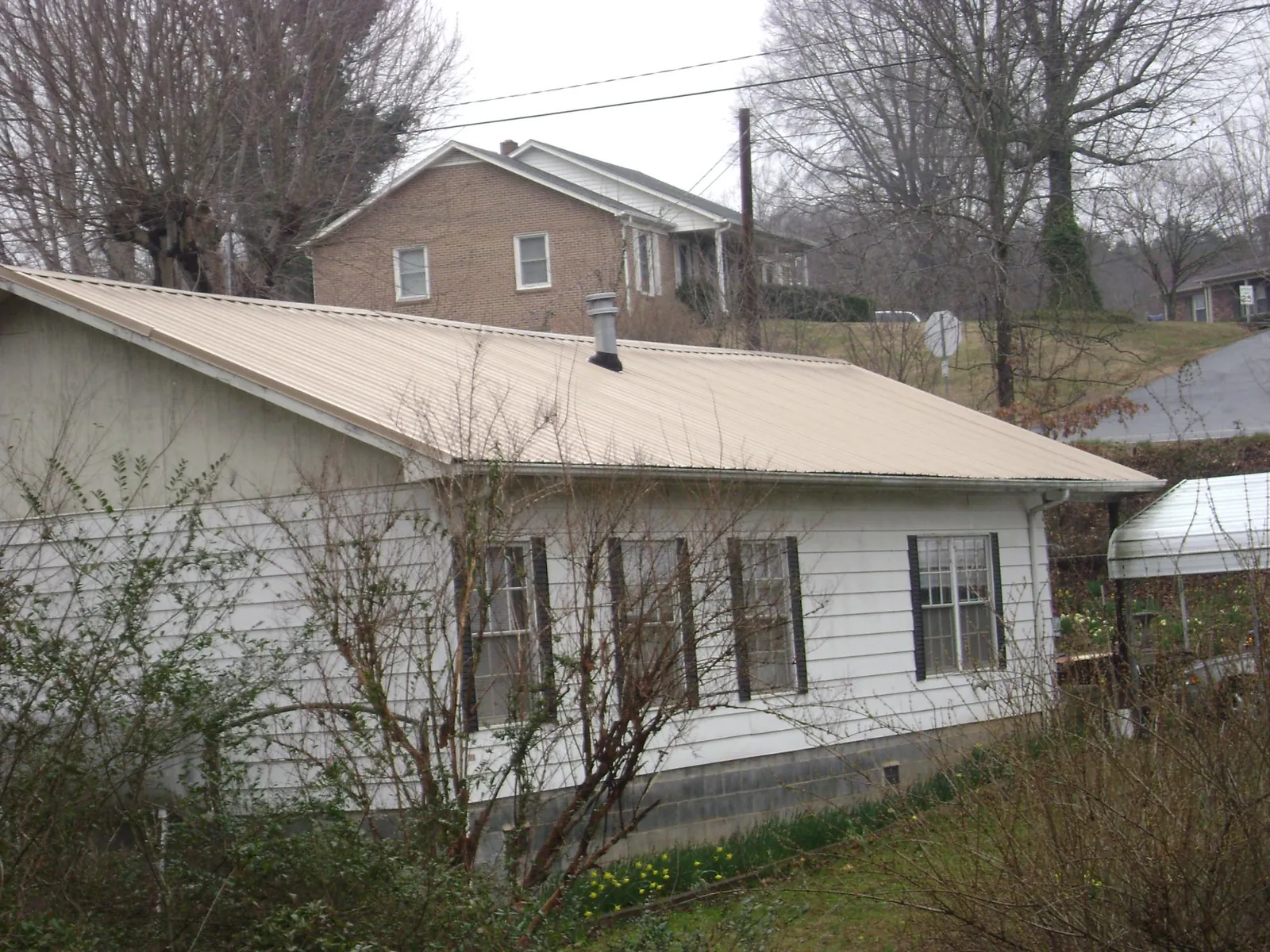 Tan metal roof on a white sided house set into a hillside — Commercial Roofing by Roofing Brothers in White Salmon
